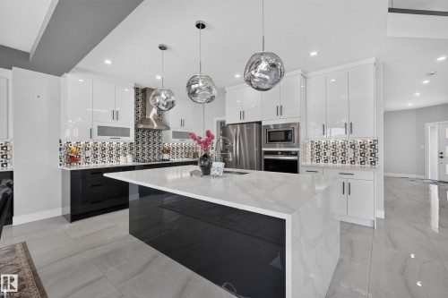 Modern kitchen featuring a waterfall island with a white countertop, high-gloss white upper cabinetry, and contrasting black lower cabinetry - 4703 41 Street, Beaumont, AB - Indoor Photo Showing Kitchen With Upgraded Kitchen