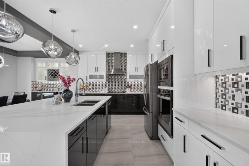 Gourmet kitchen featuring a waterfall island with a double basin sink, stainless steel appliances, and glossy white cabinetry - 4703 41 Street, Beaumont, AB - Indoor Photo Showing Kitchen With Double Sink With Upgraded Kitchen
