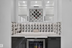 Custom wet bar featuring white upper cabinetry with glass inserts, an integrated wine rack, and a contemporary patterned backsplash - 