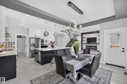 Open-concept main living area with a large kitchen island, modern pendant lighting, stainless steel appliances, a built-in fireplace feature, and light-toned tile flooring - 
