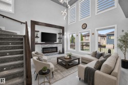 Two-story living area featuring a custom built-in media center with a stone-clad electric fireplace, wall-mounted television, and integrated shelving - 