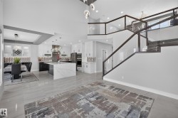 Open-concept interior featuring large format tile flooring, a contemporary kitchen with a waterfall island, high-gloss white cabinetry, and a designer backsplash - 