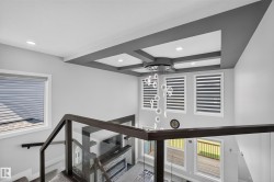 Contemporary interior featuring a coffered ceiling with recessed lighting, a multi-tier chandelier, and a glass-paneled staircase with dark wood-finish handrails - 