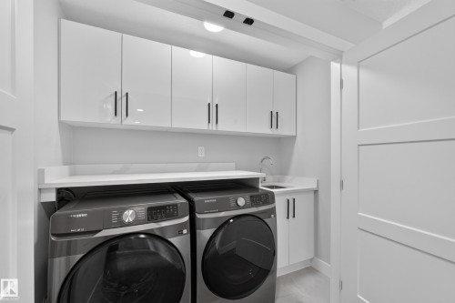 Dedicated laundry space featuring a utility sink, white cabinetry with matte black hardware, and an expansive countertop - 4703 41 Street, Beaumont, AB - Indoor Photo Showing Laundry Room