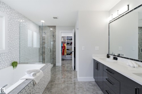 Modern bathroom featuring a dual vanity with white countertops and dark cabinetry, a large frameless mirror with integrated lighting, a spacious shower with glass enclosure, a built-in tub with mosaic tile surround, and polished floor tiling - 4703 41 Street, Beaumont, AB - Indoor Photo Showing Bathroom