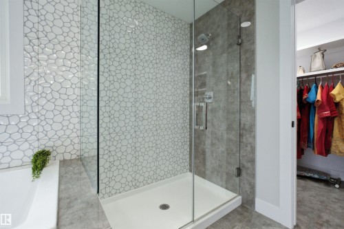 Walk-in shower featuring a glass enclosure and textured pebble-style tiling - 4703 41 Street, Beaumont, AB - Indoor Photo Showing Bathroom