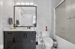 Contemporary bathroom featuring a dark grey vanity with a white countertop, a framed mirror, a modern light fixture, a toilet, and a shower with frosted glass - 