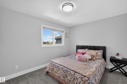 Carpeted bedroom featuring light gray walls, a flush-mount ceiling light fixture, a white-framed window, and white baseboards - 4703 41 Street, Beaumont, AB - Indoor Photo Showing Bedroom