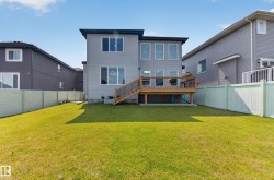 Expansive rear yard featuring a large wooden deck with stairs to the lawn, light gray horizontal siding, multiple large windows, and a light green privacy fence - 