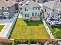 Rear exterior of a light gray residence featuring multiple windows, a second-story wood deck, and a spacious green lawn - 