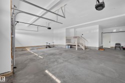 Spacious two-car garage featuring a concrete floor, white painted walls, and an accessible interior staircase with a wood railing - 