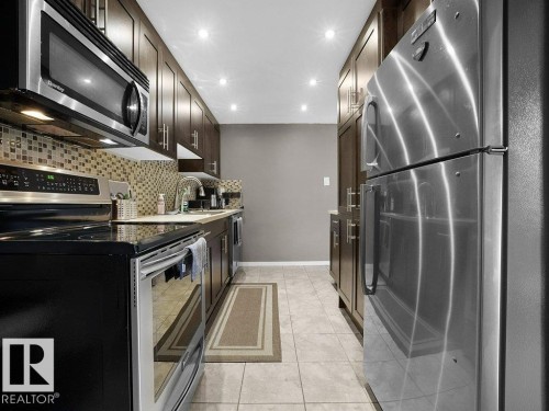 Stainless steel appliances, recessed ceiling lighting, tile flooring, mosaic tile backsplash, and dark wood-finish cabinetry - 34 Amberly Court Nw, Edmonton, AB - Indoor Photo Showing Kitchen
