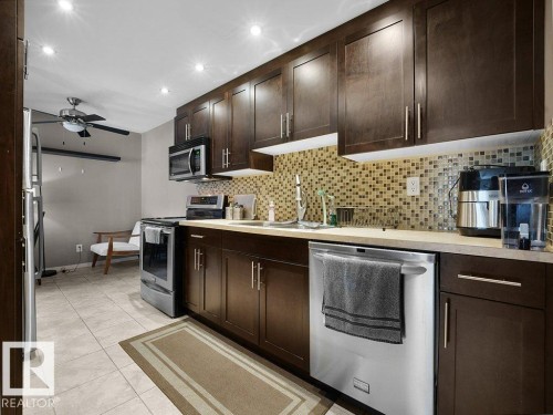 Kitchen featuring dark wood-finish cabinetry, stainless steel appliances, a mosaic tile backsplash, and light-toned flooring - 34 Amberly Court Nw, Edmonton, AB - Indoor Photo Showing Kitchen With Upgraded Kitchen