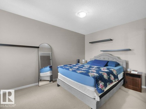 Neutral tone wall paint, flush mount ceiling light fixture, wall-mounted shelving, and carpet flooring - 34 Amberly Court Nw, Edmonton, AB - Indoor Photo Showing Bedroom