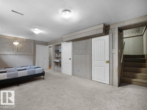 Spacious finished basement featuring neutral carpet flooring, recessed and pendant lighting, white six-panel closet doors, built-in shelving, and a wooden staircase with handrail providing access to the main level - 34 Amberly Court Nw, Edmonton, AB - Indoor