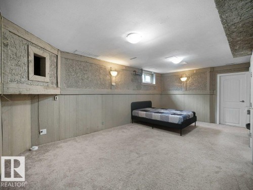Spacious finished basement featuring neutral carpet flooring, paneled walling with chair rail detail, recessed and wall-mounted lighting, and a high ceiling with accessible storage - 34 Amberly Court Nw, Edmonton, AB - Indoor Photo Showing Other Room
