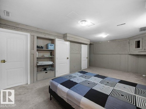 Spacious basement bedroom featuring neutral carpeting, built-in cabinetry with open shelving, and multiple white six-panel doors providing access to adjoining spaces - 34 Amberly Court Nw, Edmonton, AB - Indoor Photo Showing Bedroom