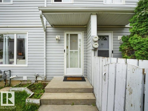 Light-colored horizontal siding exterior with a concrete entryway and white wooden fencing - 34 Amberly Court Nw, Edmonton, AB - Outdoor