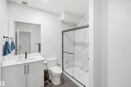 Modern bathroom featuring a floating vanity with rectangular vessel sink and matte black hardware, quartz countertop, large framed mirror with integrated lighting, marble-look tile shower enclosure with glass sliding doors, and porcelain tile flooring - 5493 Kootook Road Sw, Edmonton, AB - Indoor Photo Showing Bathroom