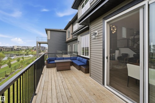 Expansive composite deck with wood-finish flooring, custom blue sectional seating, and integrated brown ottoman, overlooking manicured landscaping and open grounds - 5493 Kootook Road Sw, Edmonton, AB - Outdoor With Exterior