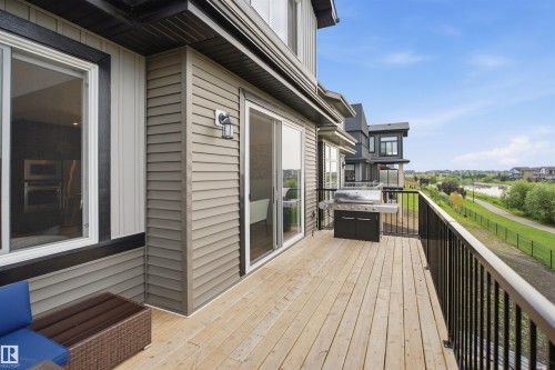 Spacious wood deck with black metal railings, sliding glass door access, and exterior wall lighting - 5493 Kootook Road Sw, Edmonton, AB - Outdoor With Exterior