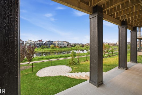 Expansive covered patio with concrete flooring, overlooking a green space, pond, and walking path - 5493 Kootook Road Sw, Edmonton, AB - Outdoor With Exterior