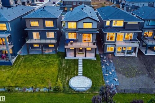 Modern residential row featuring contemporary architecture with dark exterior cladding, expansive glazing with warm interior lighting, pitched rooflines, and manicured lawn with circular hardscape feature and linear stepping stone pathway - 5493 Kootook Road Sw, Edmonton, AB - Outdoor