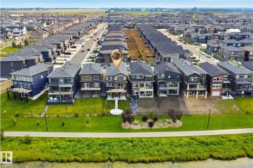 Waterfront townhome community featuring modern architectural design with multi-story construction, expansive manicured lawn, mature landscaping including trees and shrubs, and direct access to waterfront green space with integrated pathways - 5493 Kootook Road Sw, Edmonton, AB - Outdoor With View