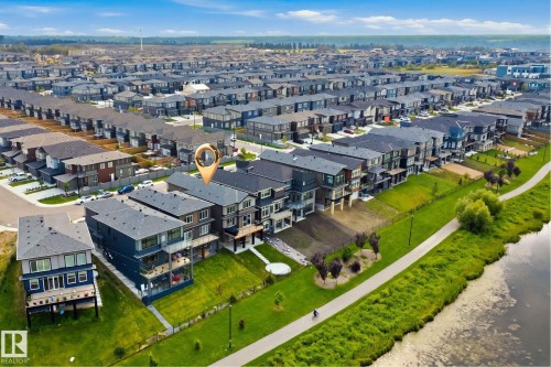 Multi-level residential structures featuring balconies, an adjacent paved pathway, and a nearby body of water - 5493 Kootook Road Sw, Edmonton, AB - Outdoor With View
