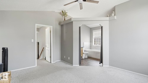 Vaulted ceiling with a ceiling fan, light gray wall paint, light-colored carpet flooring, recessed shelf feature, and an arched entry to an en-suite bathroom with a window - 4105 36A Avenue Nw, Edmonton, AB - Indoor
