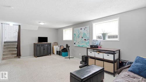 Expansive lower-level room featuring light gray walls, plush carpet flooring, two windows with white trim, and a staircase with carpeted treads - 4105 36A Avenue Nw, Edmonton, AB - Indoor