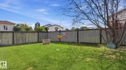 Expansive backyard featuring a lush lawn, privacy fencing, and a built-in stone fire pit - 