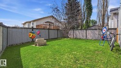 Expansive fenced backyard featuring a fire pit with stone block surround and a manicured lawn - 