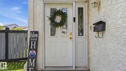 White entry door with decorative glass sidelight, brass hardware, textured exterior finish, and wall-mounted mailbox - 