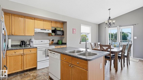Open-concept kitchen and dining area featuring wood-finish cabinetry, granite-finish countertops, stainless steel dual basin sink, and a white appliance package - 4105 36A Avenue Nw, Edmonton, AB - Indoor Photo Showing Kitchen With Double Sink