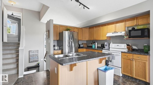 Kitchen featuring wood-finish cabinetry, dark countertops, and a double basin stainless steel sink - 4105 36A Avenue Nw, Edmonton, AB - Indoor Photo Showing Kitchen With Double Sink