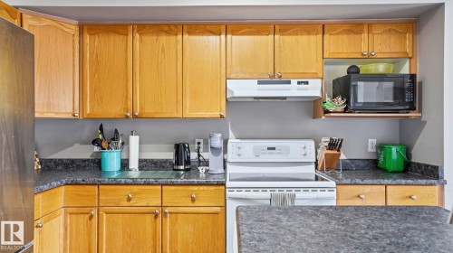 Kitchen featuring light wood cabinetry, dark speckled countertops, a stainless steel refrigerator, and a white electric range with overhead vent - 4105 36A Avenue Nw, Edmonton, AB - Indoor Photo Showing Kitchen