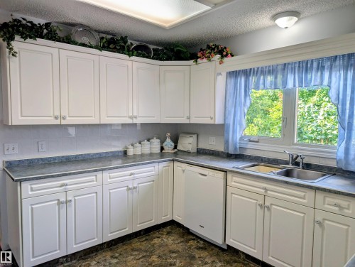 White cabinetry with clear glass knobs, a dual-basin stainless steel sink, and light gray countertops - 6014 50 Street, Vegreville, AB - Indoor Photo Showing Kitchen With Double Sink