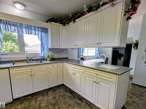 White cabinetry with silver hardware, dual basin stainless steel sink, dark textured countertops, and wood-finish flooring - 6014 50 Street, Vegreville, AB - Indoor Photo Showing Kitchen With Double Sink