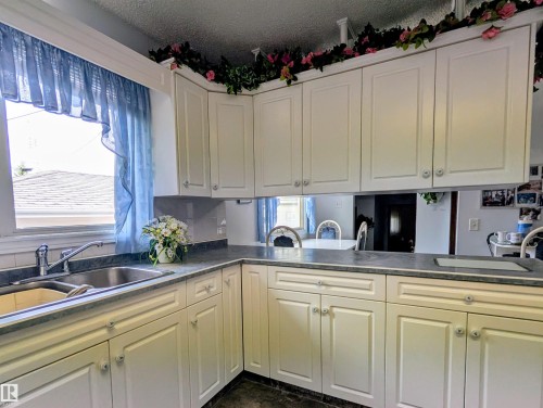 White paneled cabinetry with coordinating hardware, undermount double-basin stainless steel sink, and dark countertops - 6014 50 Street, Vegreville, AB - Indoor Photo Showing Kitchen With Double Sink