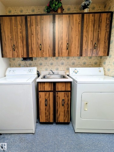 Utility sink with base cabinetry, wall-mounted cabinetry, and blue carpeting - 6014 50 Street, Vegreville, AB - Indoor Photo Showing Laundry Room