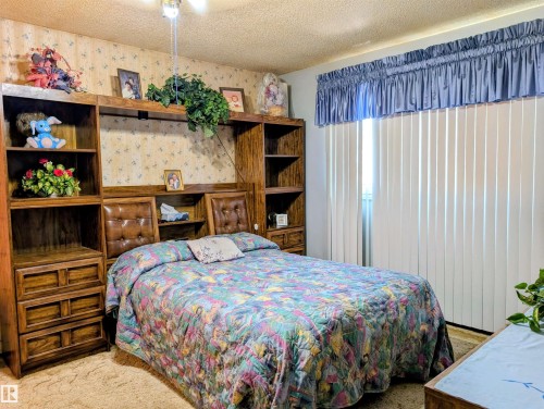 Ceiling-mounted light fixture, vertical blinds, built-in wooden shelving, and wall-mounted headboard - 6014 50 Street, Vegreville, AB - Indoor Photo Showing Bedroom