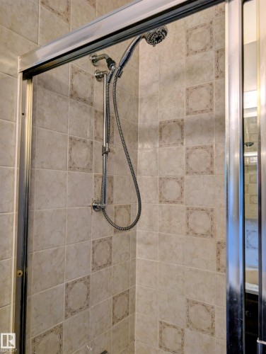 Tiled shower surround with decorative accent tiles, handheld shower fixture, and a sliding glass enclosure - 6014 50 Street, Vegreville, AB - Indoor Photo Showing Bathroom