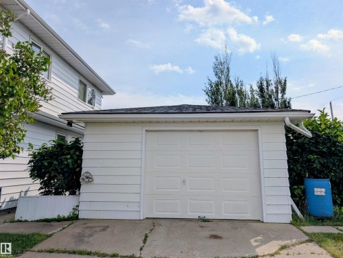 Detached garage featuring white panel siding, a white sectional garage door, white gutters, and a shingled roof - 6014 50 Street, Vegreville, AB - Outdoor With Exterior