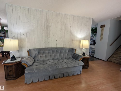 Wood-finish flooring throughout, complemented by a distressed wood-paneled wall feature - 6014 50 Street, Vegreville, AB - Indoor Photo Showing Living Room