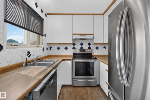 White cabinetry with wood trim, stainless steel appliances, butcher block countertops, dual basin sink, and tile backsplash - 2011 151 Avenue Nw, Edmonton, AB - Indoor Photo Showing Kitchen With Double Sink