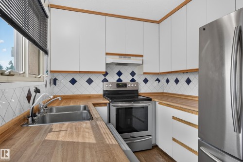 White cabinetry with wood-finish trim, stainless steel appliances, wood-finish countertops, and a double basin stainless steel sink - 2011 151 Avenue Nw, Edmonton, AB - Indoor Photo Showing Kitchen With Double Sink