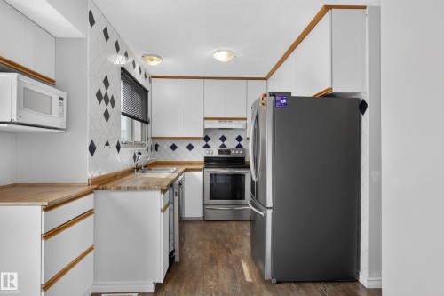 White cabinetry with wood-finish trim and handles, butcher block countertops, tile backsplash, and wood-finish flooring - 2011 151 Avenue Nw, Edmonton, AB - Indoor Photo Showing Kitchen With Double Sink