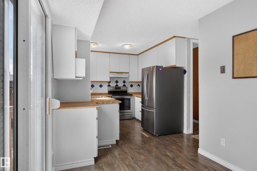 Kitchen with white cabinetry, wood-finish countertops, stainless steel appliances, and wood-finish flooring - 2011 151 Avenue Nw, Edmonton, AB - Indoor Photo Showing Kitchen