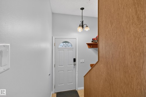 Entryway featuring a white paneled door with decorative glass, a contemporary chandelier, and wood-finish paneling - 2011 151 Avenue Nw, Edmonton, AB - Indoor Photo Showing Other Room